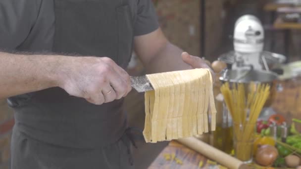 食品の背景に家庭の台所で新鮮なイタリアンパスタを作る男の料理。シェフの料理人は、伝統的なレシピでテーブルの上に手作りの生パスタを置きます。イタリア料理の自家製料理を調理. — ストック動画