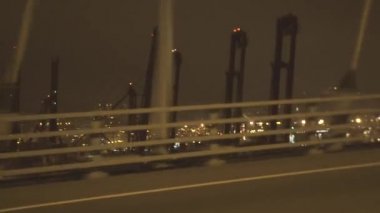 Gece şehir otobanında araba araba dan sallayarak deniz onarım limanı geçmiş. Modern şehirde deniz limanı ve binalarda endüstriyel tersane için pencere sürüş arabadan görünümü.
