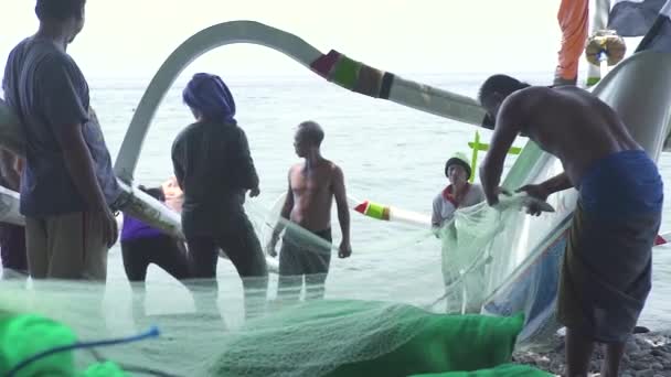 Бали, Индонезия - май 2019 года: рыбак на берегу моря ловит рыбу из рыболовной сети. Рыбаки собирают свежую рыбу из рыболовных сетей после рыбалки в океанской воде . — стоковое видео