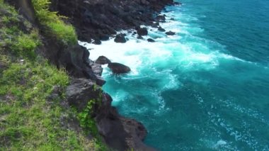Deniz dalgaları yeşil bitki arka plan üzerinde kayalık uçuruma kırma. Fırtına sırasında köpük ve sprey ile kayalık adaya sıçrayan kaba okyanus dalgaları. Dağ lık kayalıklarda turkuaz su ezilmesi.