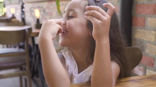 Porträt eines kleinen Mädchens, das süßen Kuchen isst und am Tisch im Café lächelt. Gesicht süße Mädchen lächeln und essen süßen Kuchen zum Dessert im Restaurant. — Stockvideo