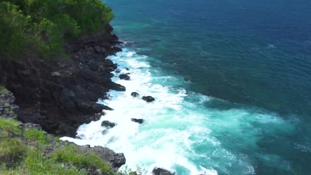 Морские волны брызгают на скалистую скалу во время шторма. Голубые океанские волны прорываются к каменистому побережью с пеной и брызгами. Размельчение бирюзовой воды на горной скале . — стоковое видео