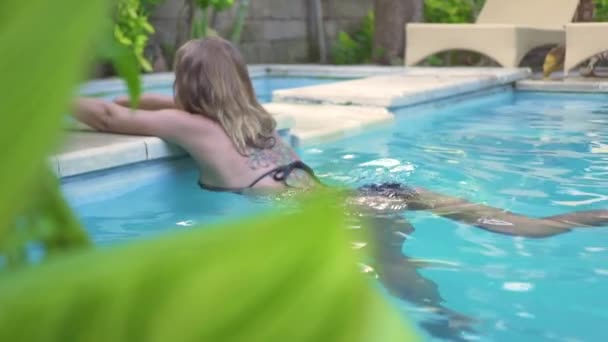 Gyönyörű nő pihentető kék víz medence nyári üdülőhelyen. Vonzó nő fekete bikini szabadtéri medencében nyári vakáció. Üdülés életmód — Stock videók