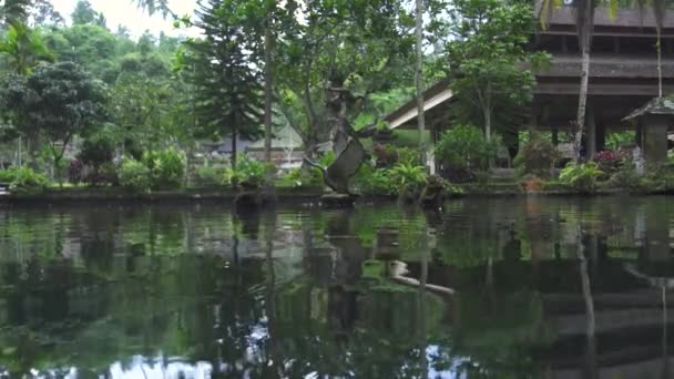 緑の庭の風景の装飾的な魚の池でインドネシアの神像。インドネシアのバリ島にある古代の伝統的建築。アジアの文化。旅行コンセプト. — ストック動画