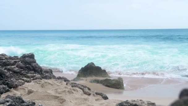 Tengervíz hullámok fröccsenő homokos tengerpart táj. Türkiz óceán Látóhatár táj. Sziklák a homokos strandon. — Stock videók