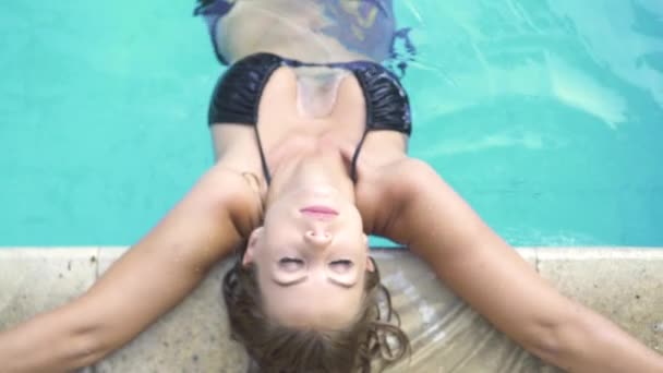 Gebräunte Frau entspannt sich im blauen Schwimmbad im Sommerferienort. schöne Frau im schwarzen Bikini im Außenpool. Sommerferien. Urlaubsstil. — Stockvideo