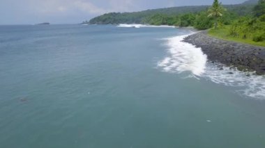 Havadan mavi deniz dalgaları ve yeşil tropikal ada manzara görünümü. Drone yeşil adada kayalık kıyı şeridi üzerinde sıçrayan mavi okyanus dalgaları görünümü. Bali, Endonezya.