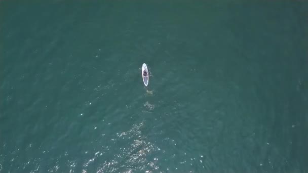 Man riding on stand up paddle board on sea waves at summer vacation. Aerial view. Athlete man surfing on SUP board with rowing oars in blue ocean. Water sport. Extreme sport. Summer activities. — Stock Video