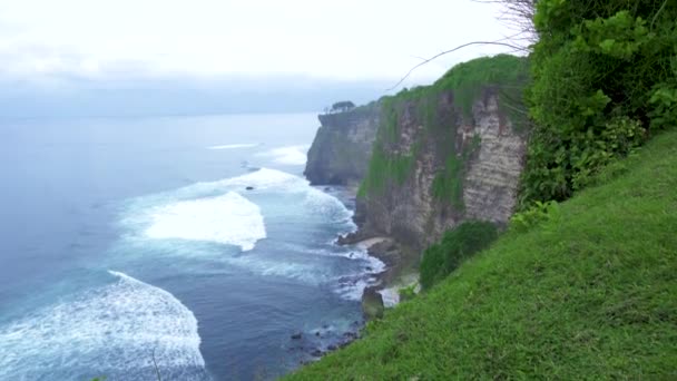 Bergsklippa på kusten och stänk havsvågor. Amazing landskap Cliff Mountain och Rocky Island på Blue Ocean Shore. Vacker utsikt över den klippiga ön. Bali, Indonesien. — Stockvideo