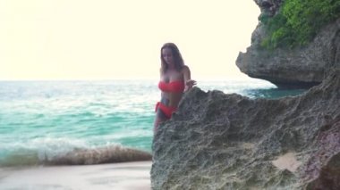 Baştan çıkarıcı kadın kayalık plaj ve deniz dalgaları arka yürüyüş. Tropik yaz sahilinde mayo giyen çekici kadın. Tropik tatil. Tatil yaşam tarzı.