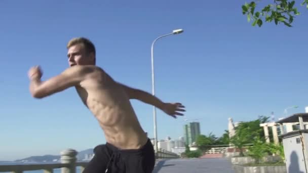 Young man training parkour jump in summer park. Athlete man doing acrobatics stunt and trick on sea background. Active youth lifestyle. Adrenaline sport training. Extreme sport. Workout outdoor. — Stock Video