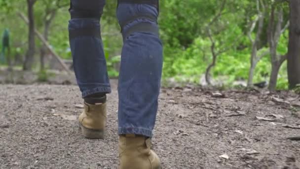 Motorcyclist man in jeans and moto outfit walking on countryside road. Motorbiker in moto clothes back view, low angle view. — Stock Video