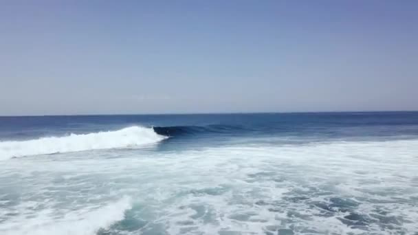 Captura aérea de seguimiento de un surfista que monta grandes olas de surf en el océano azul profundo en el día — Vídeos de Stock