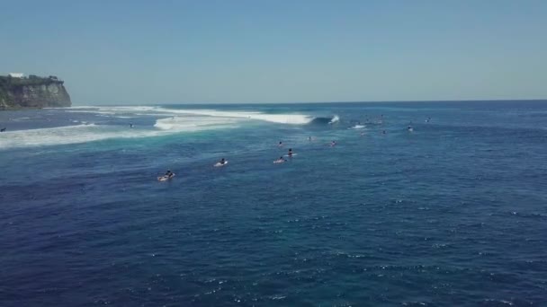 Drone view over blue ocean full of surfers enjoys paddling and riding waves. — Stock Video