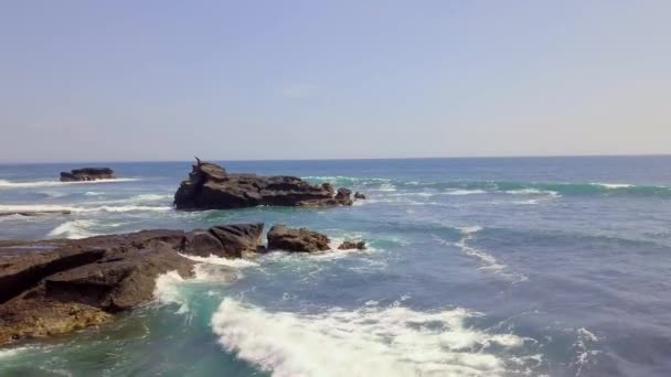 Vzdušný výhled na skalnaté pobřeží a vlnitý modrý oceán. Bílé vlny padají. — Stock video