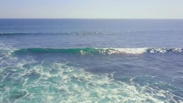 Luftaufnahme über eine felsige Meeresküste und einen welligen blauen Ozean. Weiße Wellen stürzen ab. — Stockvideo