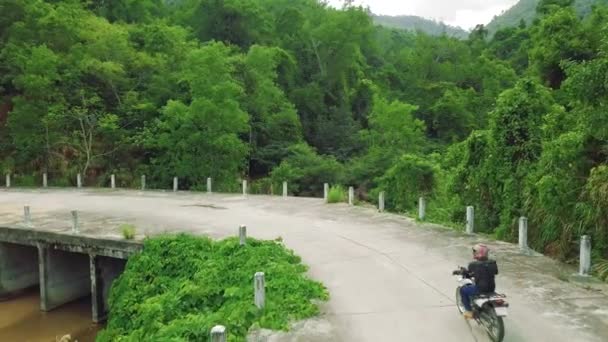 Flygfoto av en motorcykel ryttare körcykel längs en bro på landsbygden. — Stockvideo