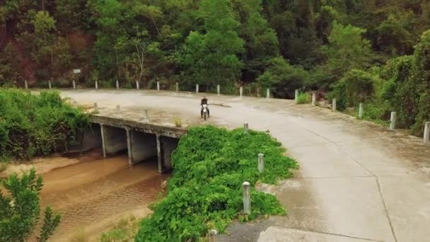 Повітряний вид на мотоцикліста з парковкою на велосипеді на мосту в джунглях річки. — стокове відео