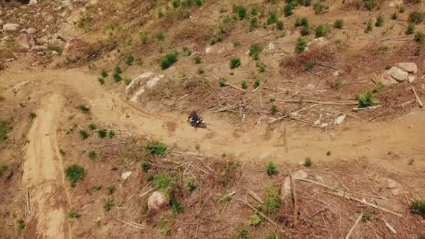 Aerial view of motorcyclist ride on dirt road in the mountains down hill. — Stock Video