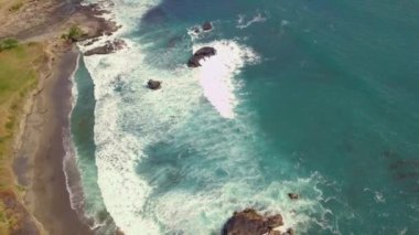 Kayalık bir deniz kıyısı ve dalgalı mavi bir okyanus üzerinde hava manzarası. Beyaz dalgalar çarpıyor.