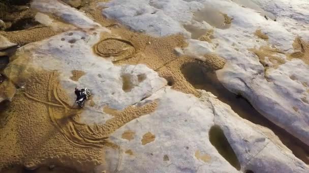 Воздух: Dirtbiker экстремальная поездка на автомобиле по асфальтированному камню с песком в реке . — стоковое видео