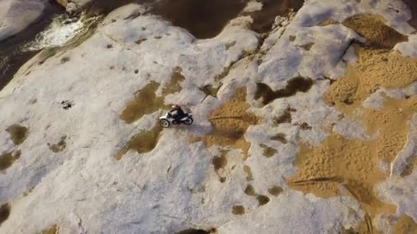 Letecký záběr člověka v řece, zatímco dělá kaskadérské kousky na špinavém kole na pískovcové dlážděné kámen — Stock video