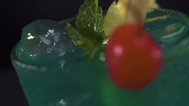 Un bicchiere di cocktail verde con ciliegie, ananas e foglie di menta che ruotano lentamente — Video Stock