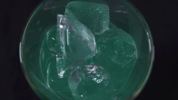 검은 바탕에 얼음을 넣은 유리잔에 녹색 칵테일을 붓는 남비. — 비디오