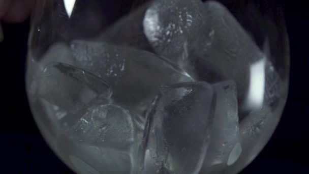 Um uísque derramado em um copo transparente com cubo de gelo no fundo escuro . — Vídeo de Stock