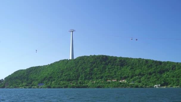 Een groen eiland in de bue zee met antenne tramlijn pyloon en bewegende kabelbanen. — Stockvideo