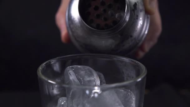 Barmans hand gieten groene cocktail van een shaker naar een glas vol ijs. — Stockvideo