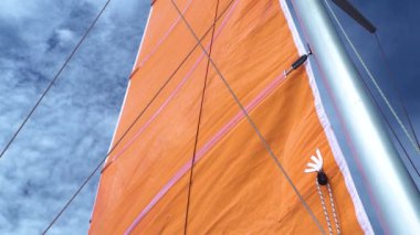 Yazın mavi gökyüzüne karşı yatın turuncu ana yelkenli manzarası.