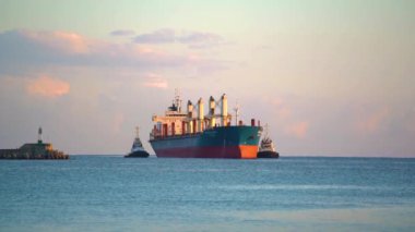 Sakin denizde hareket eden ve limandan ayrılan büyük bir kargo gemisinin görüntüsü..