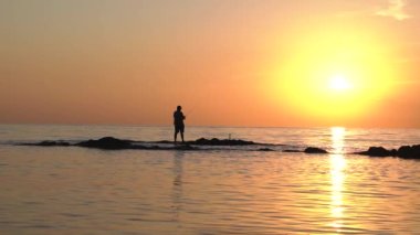 Okyanusta gün batımının manzarası. Balık yakalayan bir adamın silüeti..