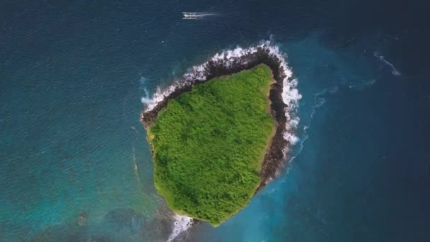 岩の上に波がクラッシュして緑豊かな緑の完全な小さな島の上にドローンビュー. — ストック動画