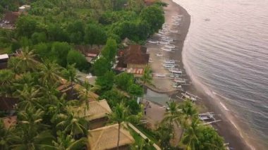 Villa, tekne ve yeşillik manzaralı tropikal sahil beldesi üzerinde İHA uçuşu.