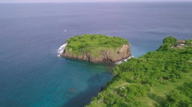 İHA, yeşil bir uçurum ve mavi denizde yeşil bir adacık üzerinde uçuyor..
