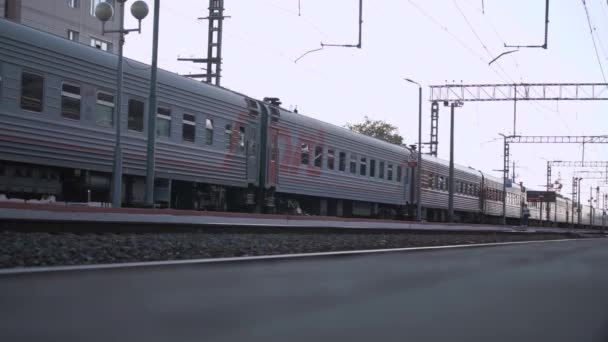Dlouhý šedý osobní vlak jede po kolejích kolem nástupiště — Stock video