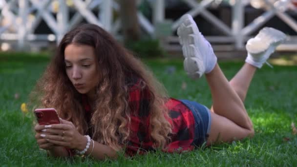 Lang haar brunette op groen gras en kijkt in mobiele telefoon — Stockvideo