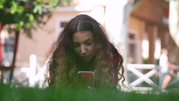 Junge Frau liegt auf grünem Rasen und lächelt langsam — Stockvideo