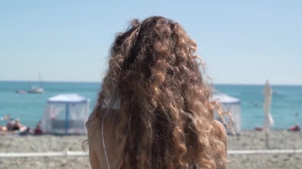 Елегантна жінка з коричневим кучерявим волоссям стоїть на березі — стокове відео