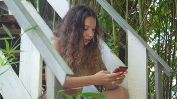 Νεαρή γυναίκα με μακριά σγουρά μαλλιά σε κόκκινο smartphone — Αρχείο Βίντεο