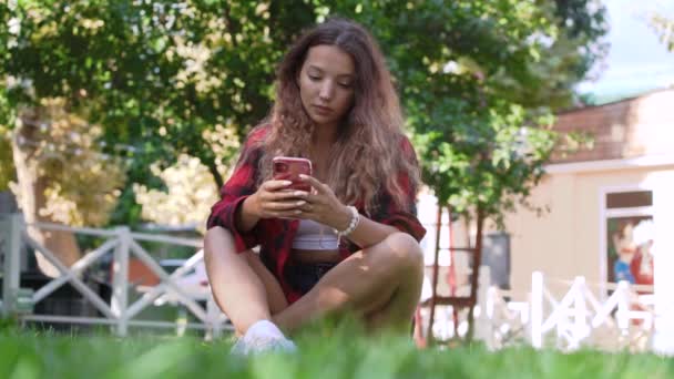 Lady glättet lange lockige Haare und tippt auf rotem Smartphone — Stockvideo