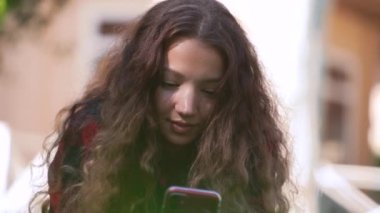 Kıvırcık saçlı genç bir kadın akıllı telefon ekranına bakar.