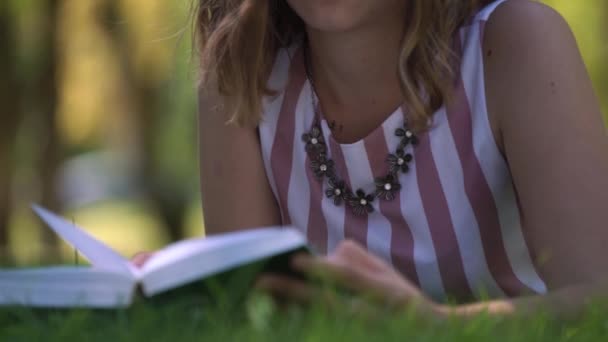 Rubia de pelo rizado se encuentra en la hierba verde y lee libro — Vídeo de stock