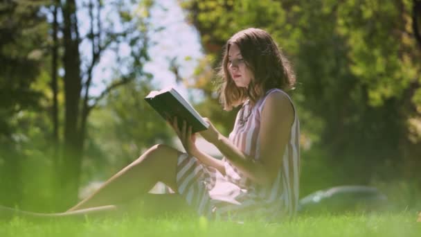 Saçları açık genç bir kadın parkta kitap sayfalarını çeviriyor. — Stok video