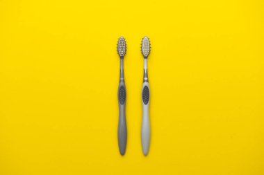 Sarı arka planda iki farklı gri diş fırçası.