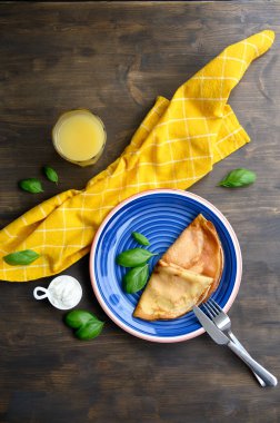 Fesleğen yaprakları ve ahşap bir masada sarı peçeteyle süslenmiş mavi bir tabakta etli ve ekşi kremalı krep. Düz yatıyordu.