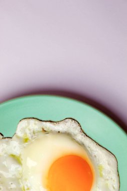 Pastel yeşil bir tabakta sahanda yumurta, pastel mor bir arka planda. Yakın plan.