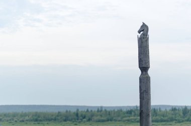 Yakut pole with a horse Serge stands with the head of a horse made of wood on a cliff on the background of endless tundra and forest under the clouds.  clipart